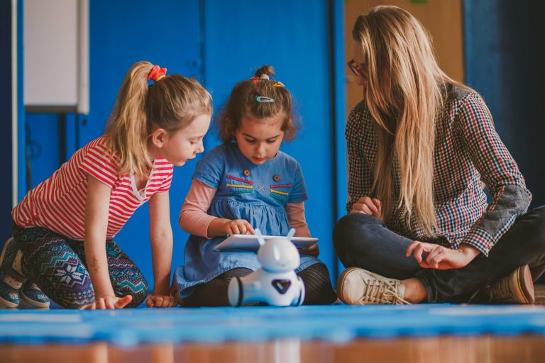 Op deze afbeelding zie je twee kinderen en een volwassenen met een iPad op de grond.
