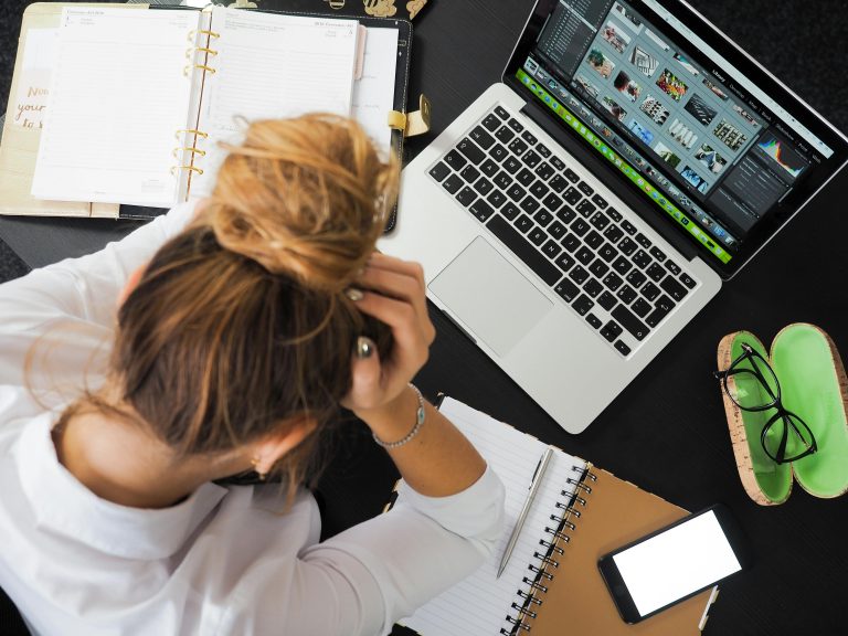 Vrouw zit met handen in het haar achter de laptop